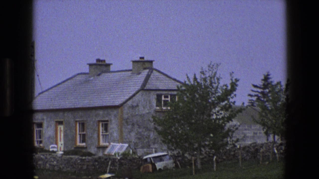 1969 England 8mm frame of a rural stone cottage behind a low wall, seen through dark vertical framing.