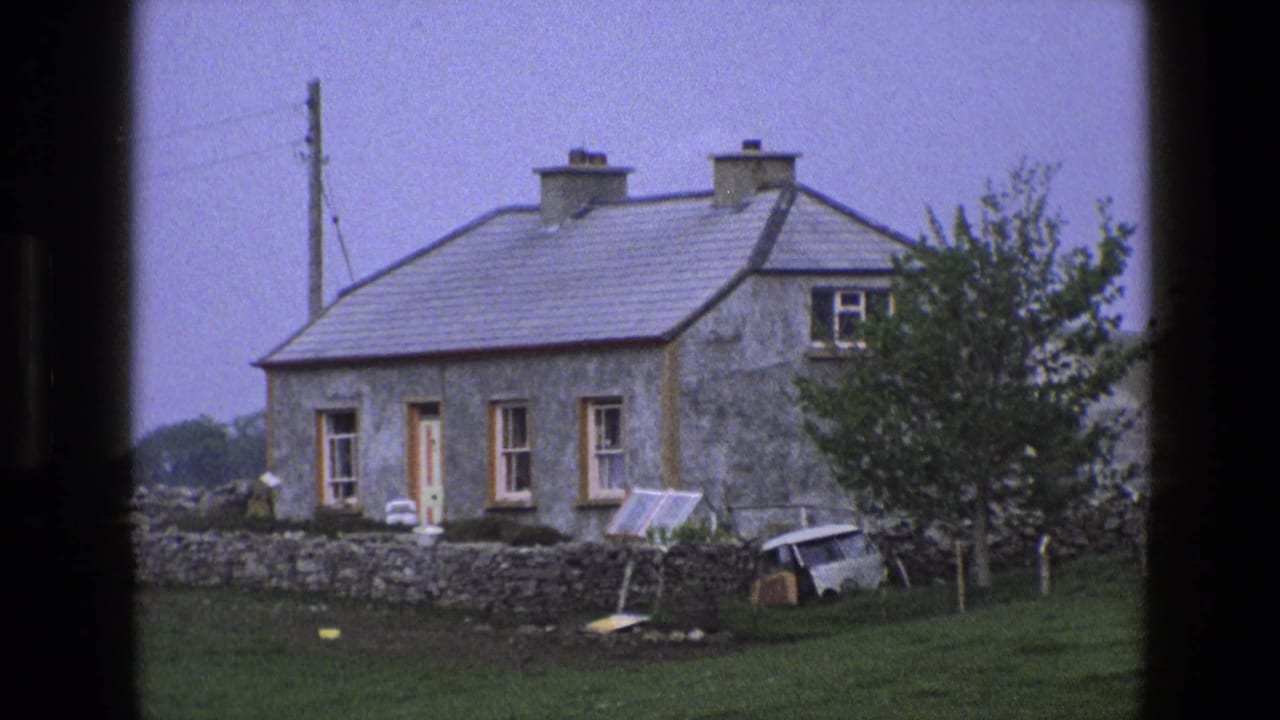 1969 England 8mm frame showing a stone cottage, yard wall, small van, leaning panel, and trees in a rural setting.