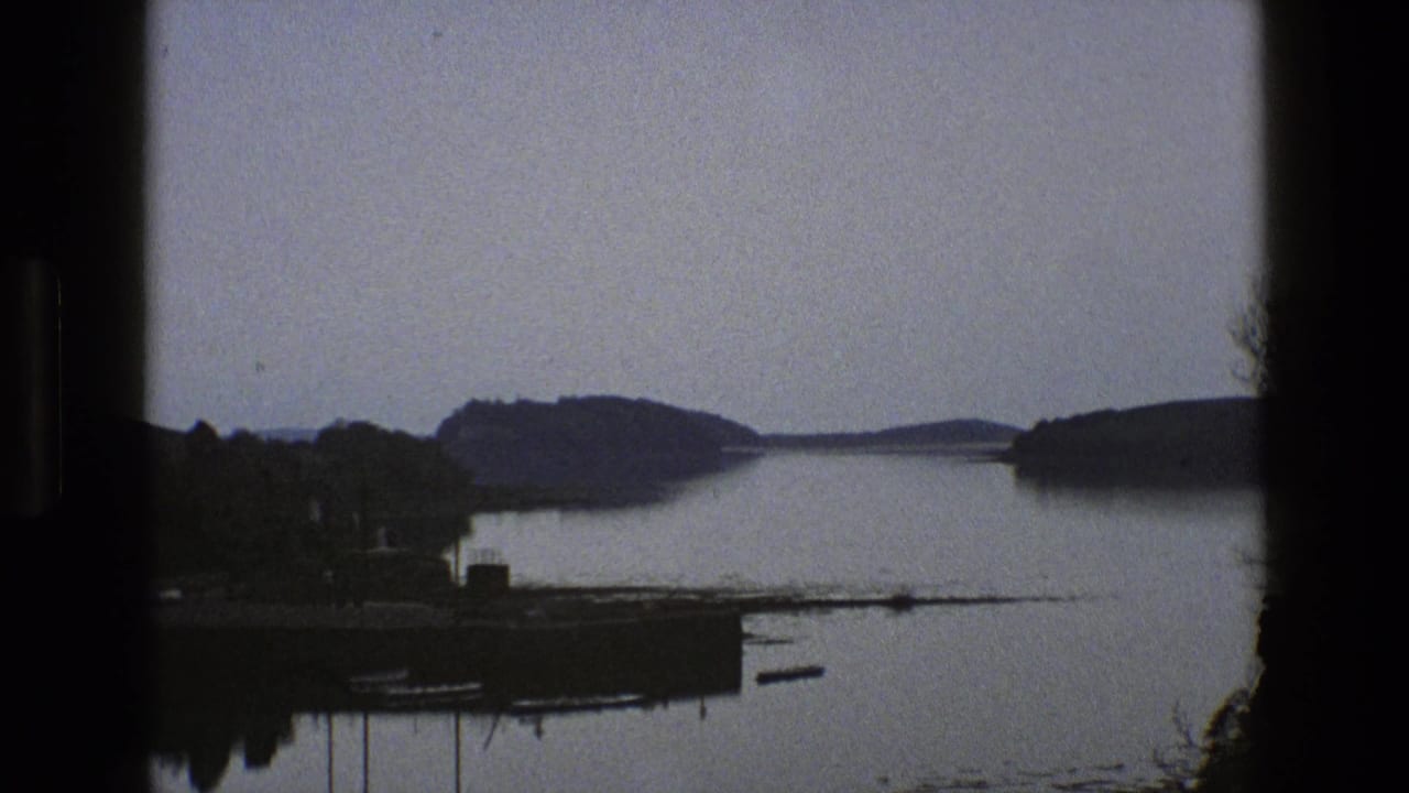 Wide lake view with a small shoreline landing, wooded banks, and distant hills.