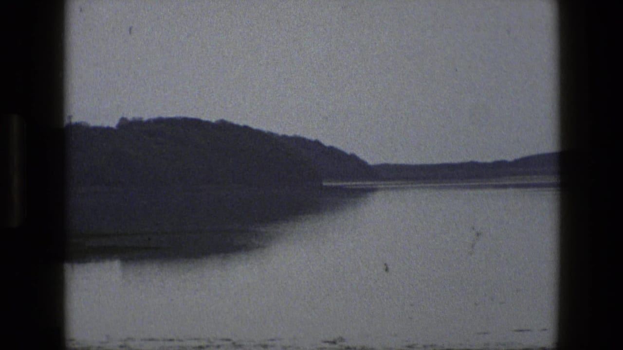 1969 England home-movie frame showing dark hills beyond still water under a grey sky.
