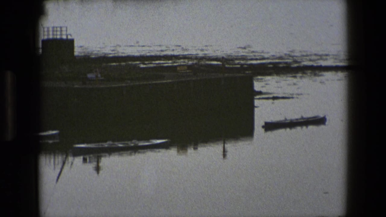 1969 England harbor view with small boats moored near a stone pier and still water under an overcast sky.