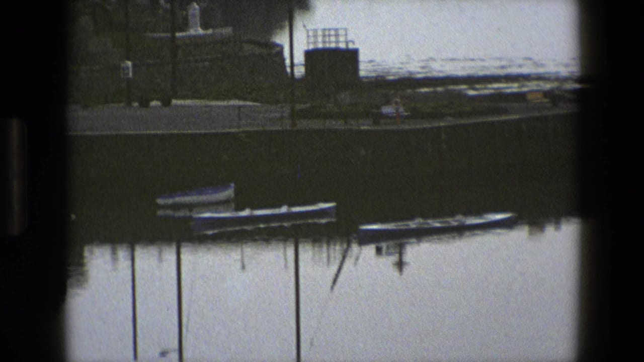 Harbor quay with several small boats, mooring posts, shoreline structures, and still water.