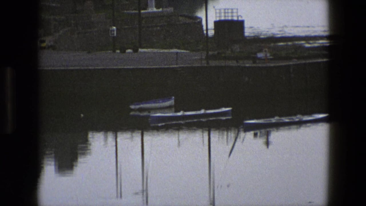 1969 England 8mm frame showing small moored boats and their reflections in still water under dark pier or window framing.