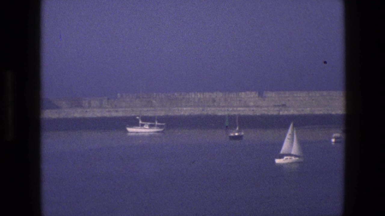 1969 England 8mm frame showing anchored sailboats on a hazy bay, seen through a dark window frame.