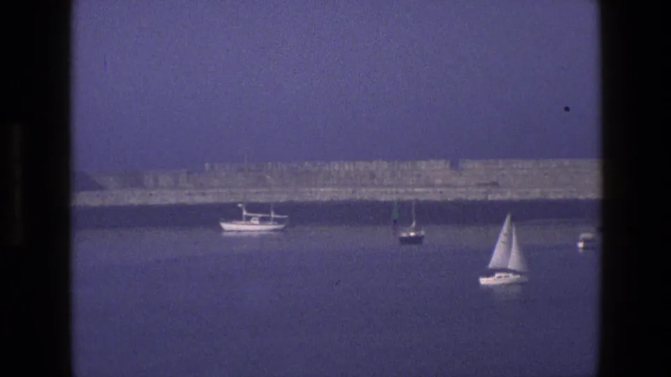 1969 England 8mm frame showing anchored sailboats on a hazy bay, seen through a dark window frame.