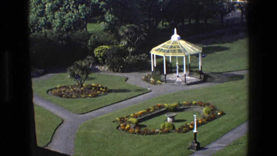 1969 England 8mm closing frame of the garden, showing the gazebo, patterned paths, flowerbeds, lawns, and distant visitors.