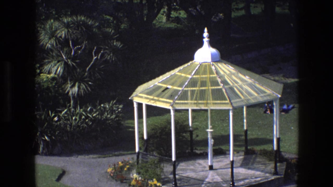 1969 England park scene with a yellow-roofed bandstand, formal paths, lawns, trees and small distant visitors.