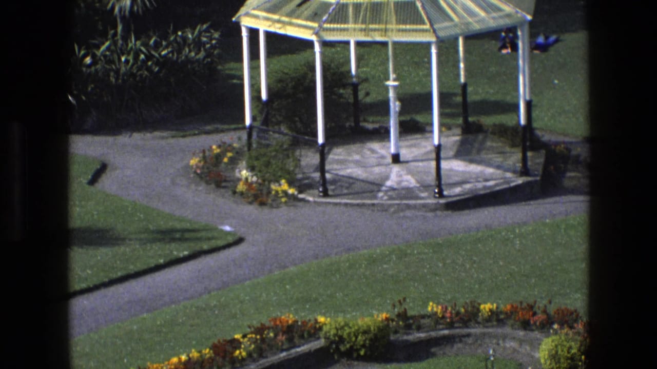 Gazebo and intersecting garden paths with lawn and flowerbeds in sunlight.
