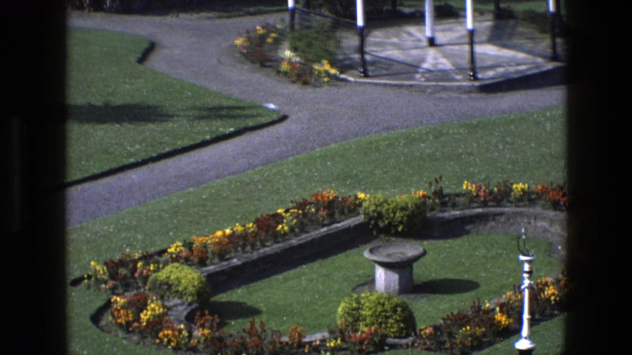Manicured garden with flowerbeds, lawns, paved paths, and a stone birdbath.