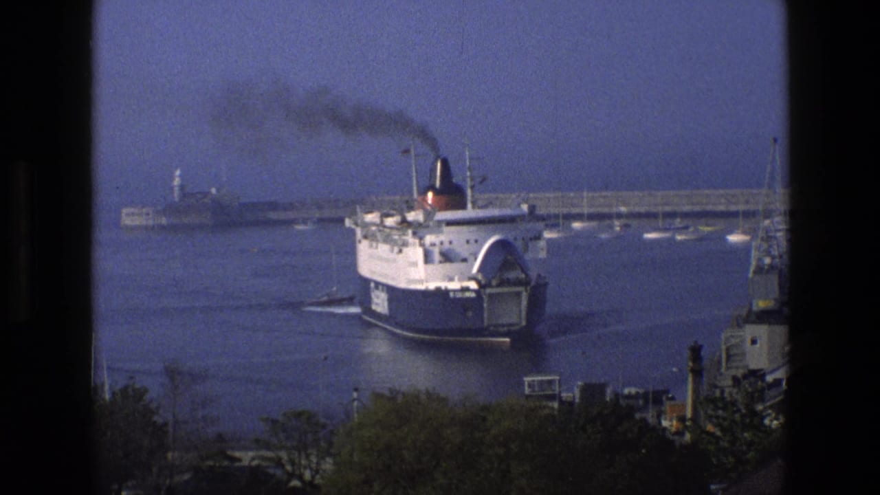 1969 England 8mm frame showing the SeaLink ferry St Columbia approaching harbor water with smoke trailing from the funnel.