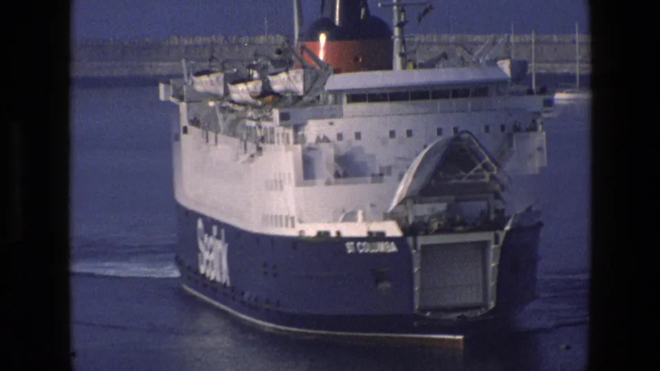 Close 8mm frame of the St Columbia ferry in harbor, emphasizing the open stern ramp, blue hull, and SeaLink vessel markings.