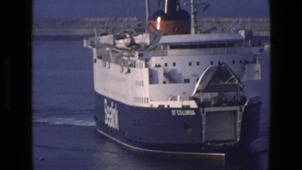 The St Columba ferry appears closer in the harbor, showing its blue hull, white upper decks, stern ramp, and visible Sealink branding.