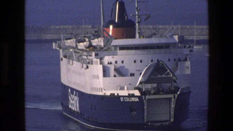 A closer 8mm view of the St Columba ferry shows lifeboats, white upper decks, red funnel, stern ramp, and the vessel name on the hull.