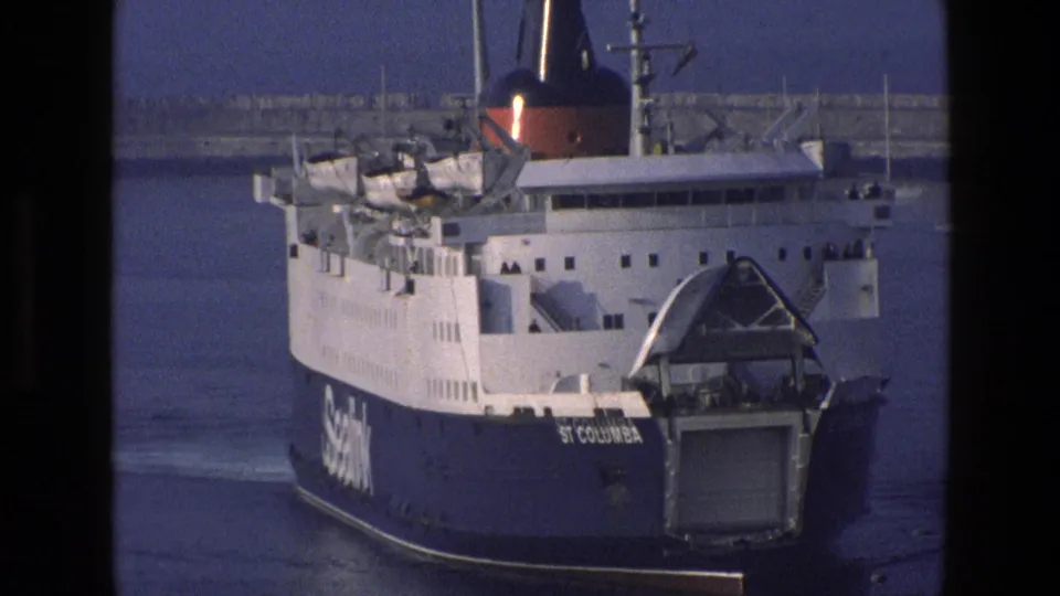 The ferry St Columba continues through calm harbor water in 1969 England footage, framed by dark 8mm gate edges and a visible vertical splice area.