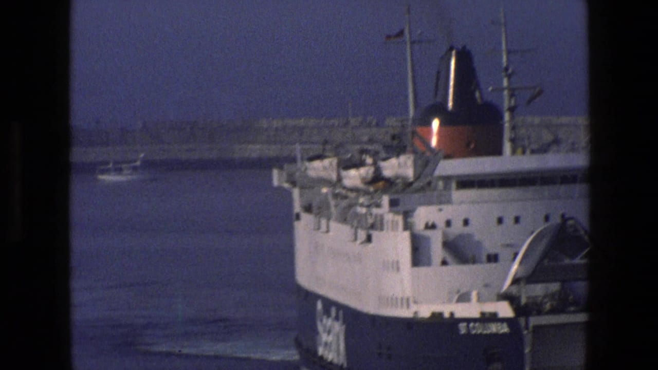 Large ship docked at a harbor with water and shoreline in the background.