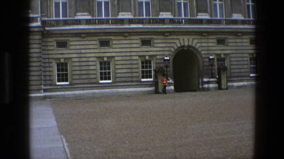 1969 England 8mm frame with a wide view of a formal palace courtyard, guards at posts, and an arched stone entrance.