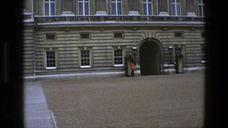 1969 England 8mm frame showing a Queen's Guard at attention near a sentry box outside a stone palace facade.