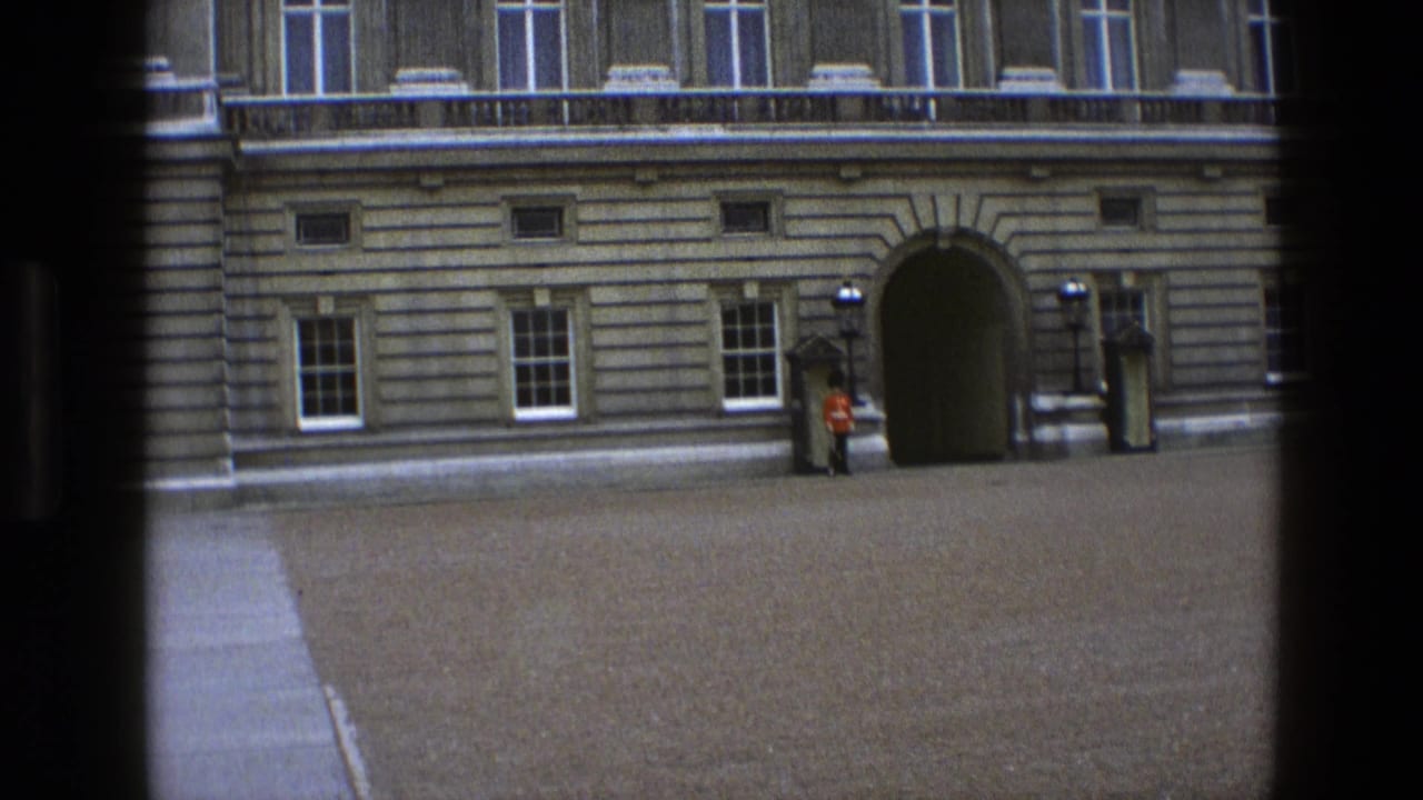 1969 England home-movie frame with a ceremonial guard standing still beside the palace entrance and sentry box.