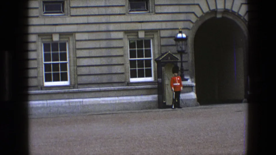 Closer 1969 England 8mm view of a Queen's Guard standing at attention outside a formal stone building.