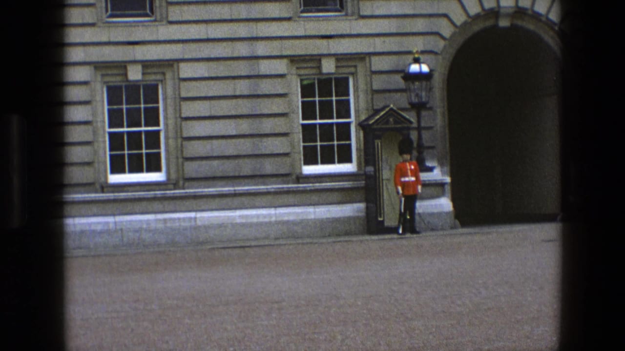 1969 England home-movie frame showing a British ceremonial guard in red tunic standing by a sentry box at a stone building entrance.