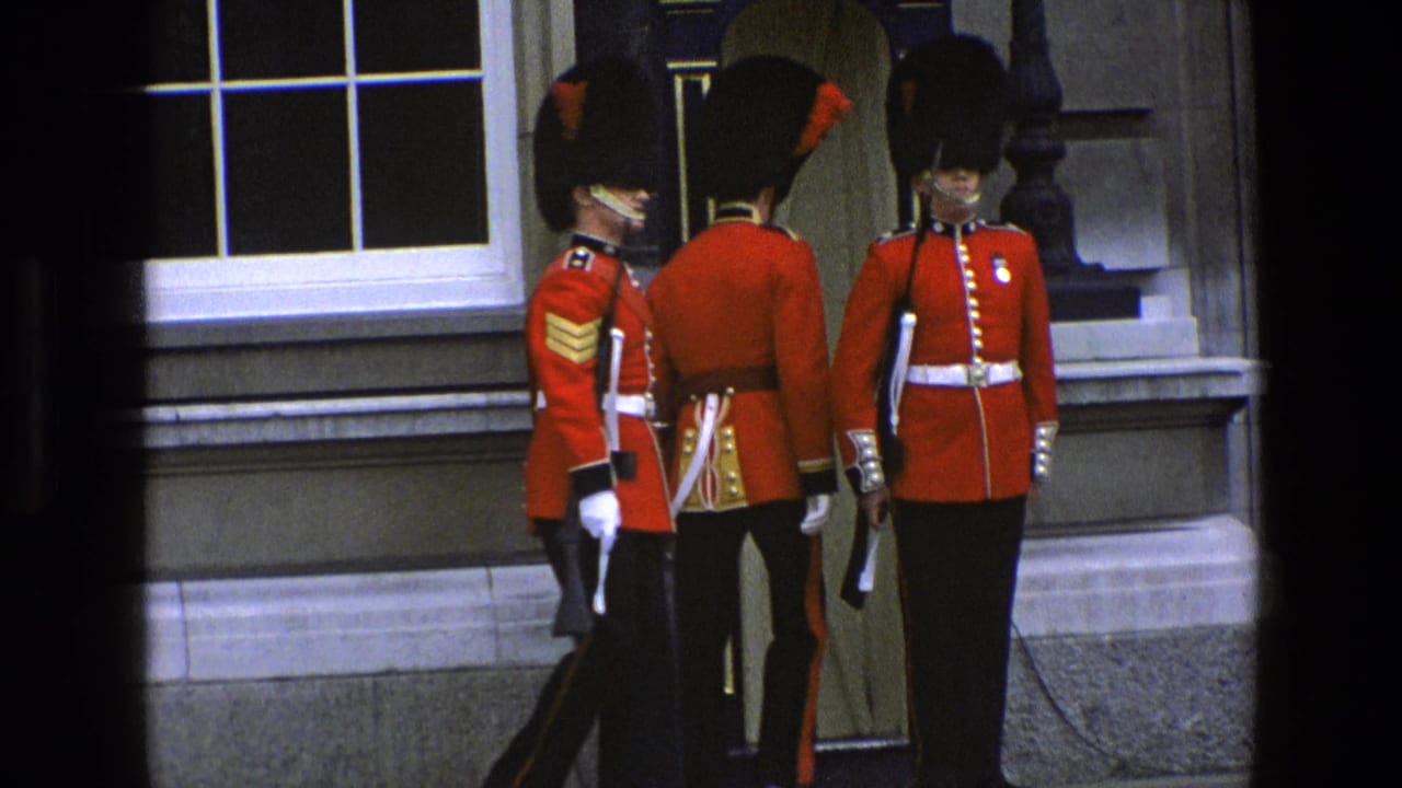Three guards in red tunics and bearskin hats stand near a sentry box outside a stone building.