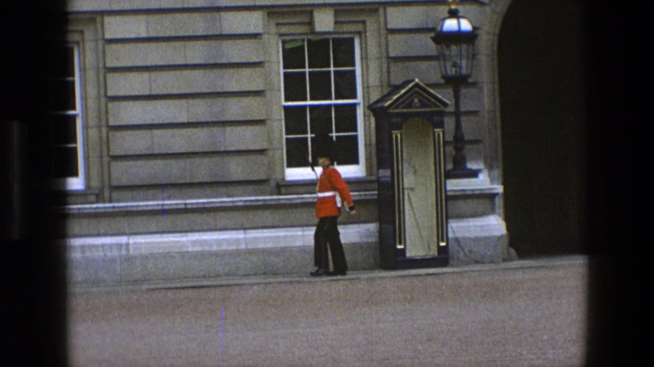 1969 England 8mm frame of a red-coated guard beginning a ceremonial patrol beside a sentry box and stone wall.