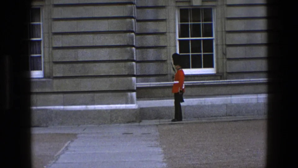 At the end of the 1969 England clip, the ceremonial guard appears stopped beside the stone facade, holding position near a window.