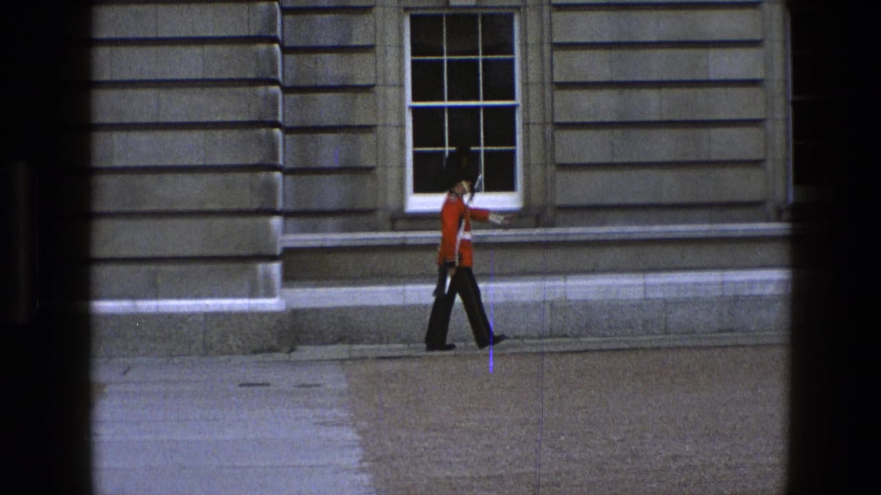 Guard in red tunic marches along a stone wall while carrying a rifle.
