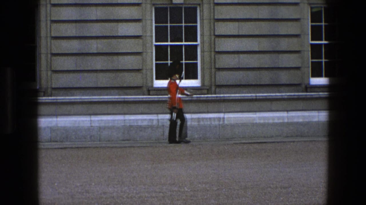 In 1969 England footage, a guard in red tunic and tall black hat marches beside a stone facade with sash windows.