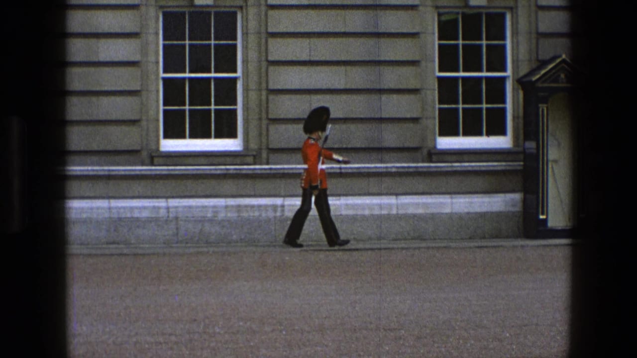 Guard in red uniform walking toward a sentry box beside stone windows.