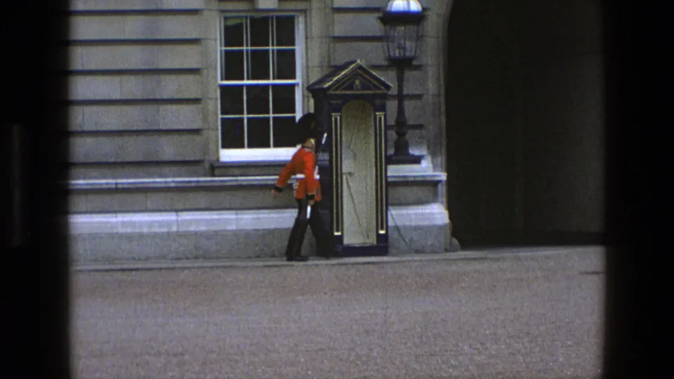 A ceremonial guard reaches the sentry box area, partly framed by dark window edges and the stone building behind.