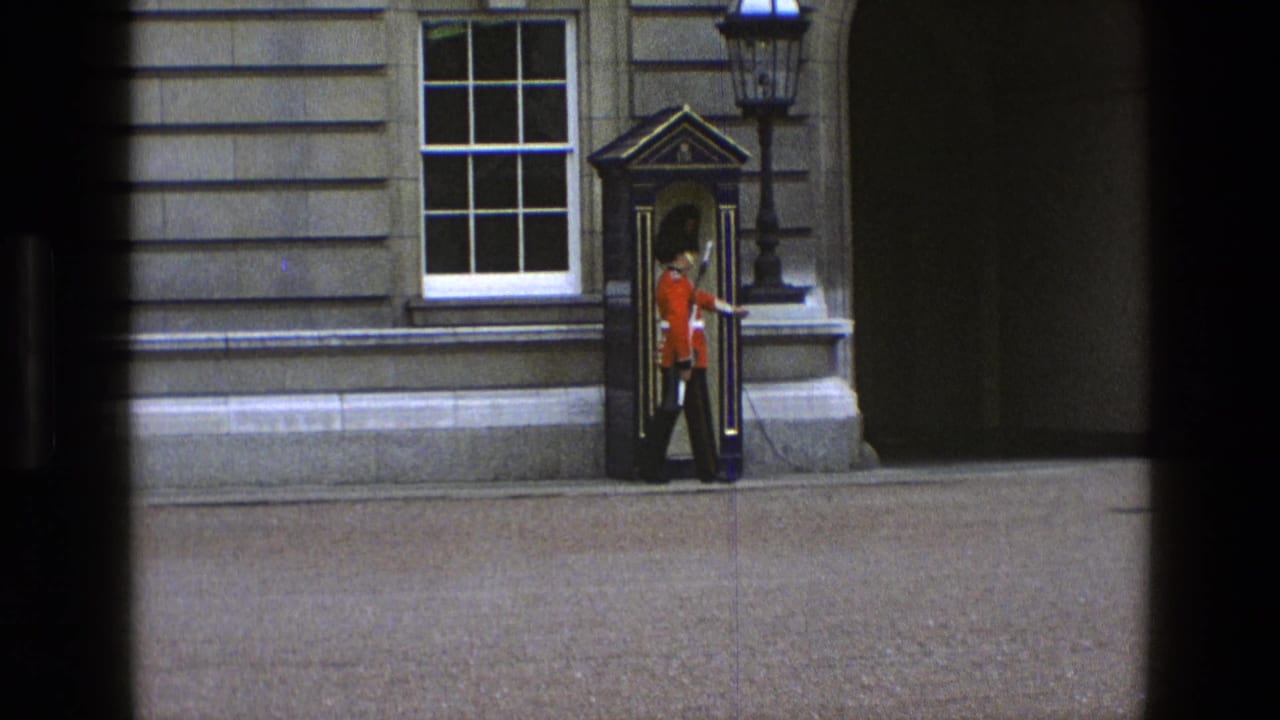 Red-uniformed guard stands beside a sentry box against a stone building.