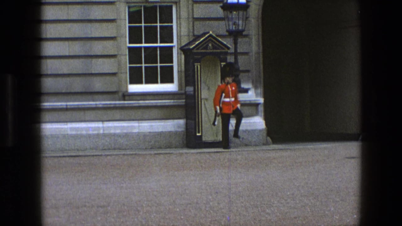 A British ceremonial guard appears to step from the sentry box during a formal turn beside the stone building.