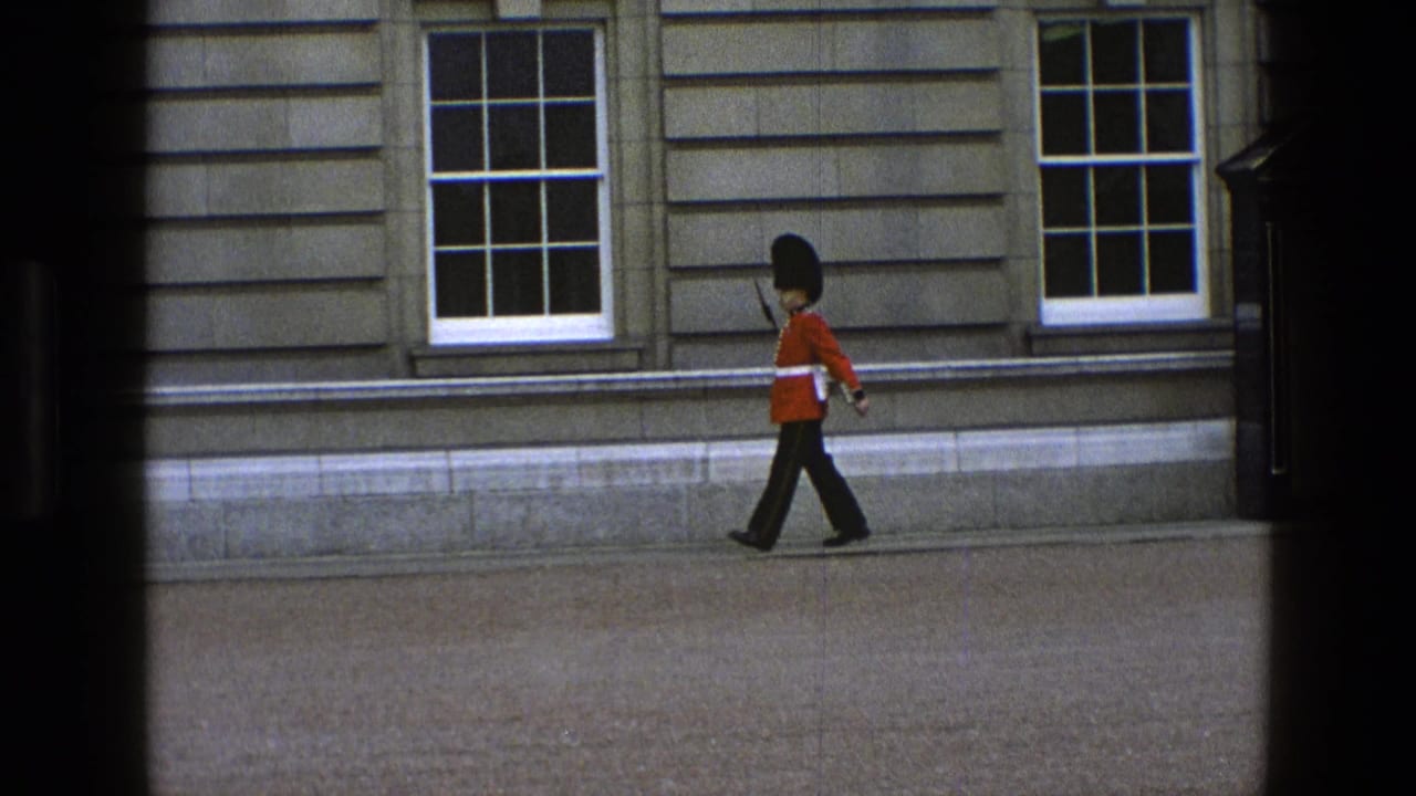 Guard in red tunic marching along a stone building facade.