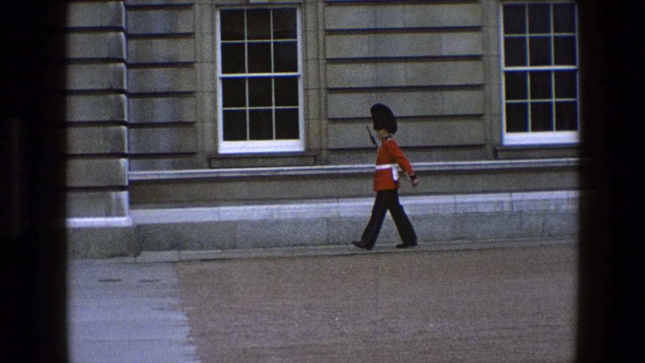 In 1969 England footage, a Queen's Guard in red tunic and tall black hat walks along a stone facade with sash windows.
