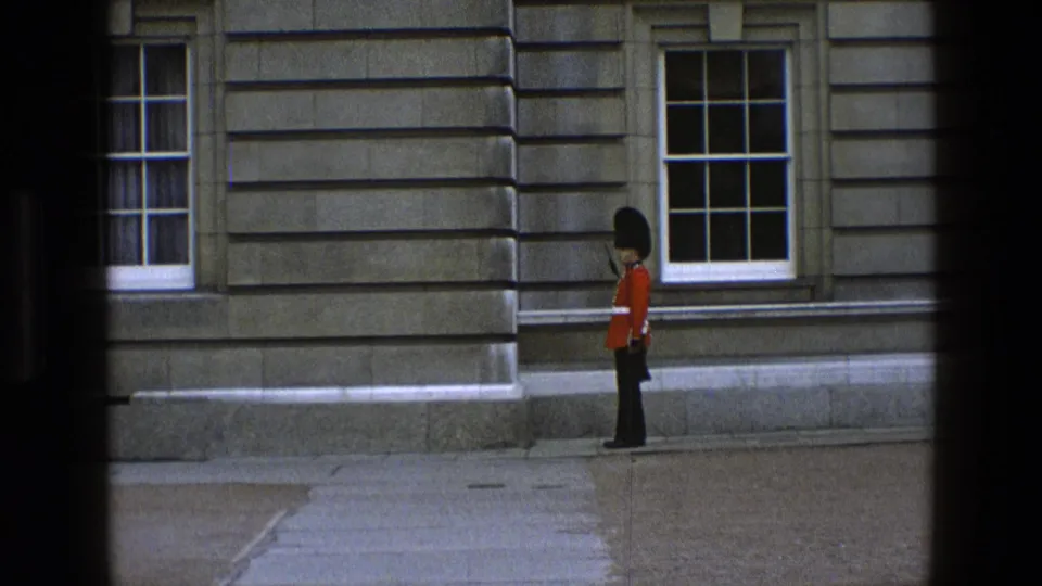 The guard is seen near the center of the 8mm frame, standing or stepping beside a stone building and tall window.