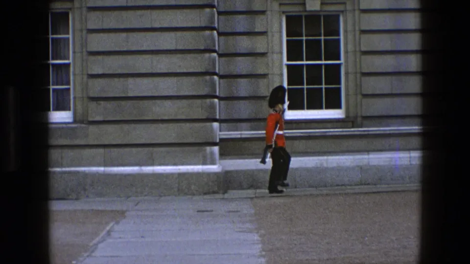 The final frame shows the ceremonial guard continuing along the pavement beside a stone facade and sash window.