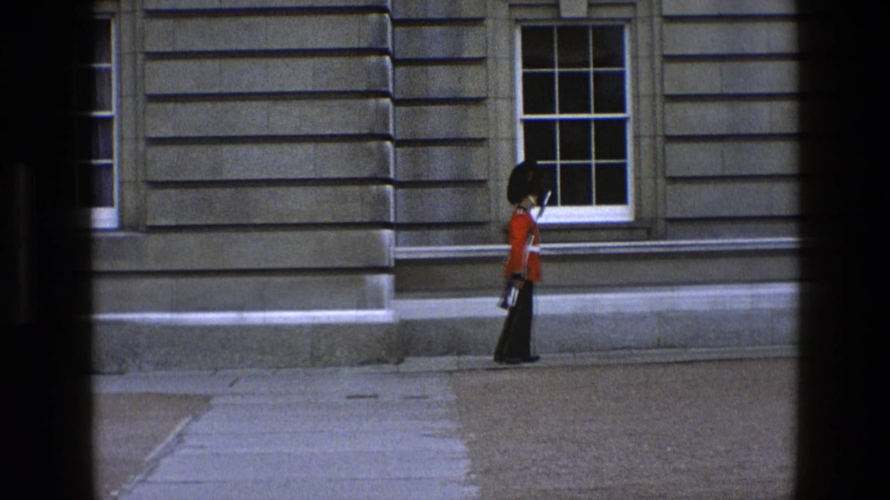 Royal Guard in red tunic marching beside a stone building with sash windows.