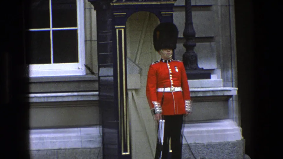 1969 England frame showing a closer view of the royal guard at attention, with sentry box and stone facade behind.