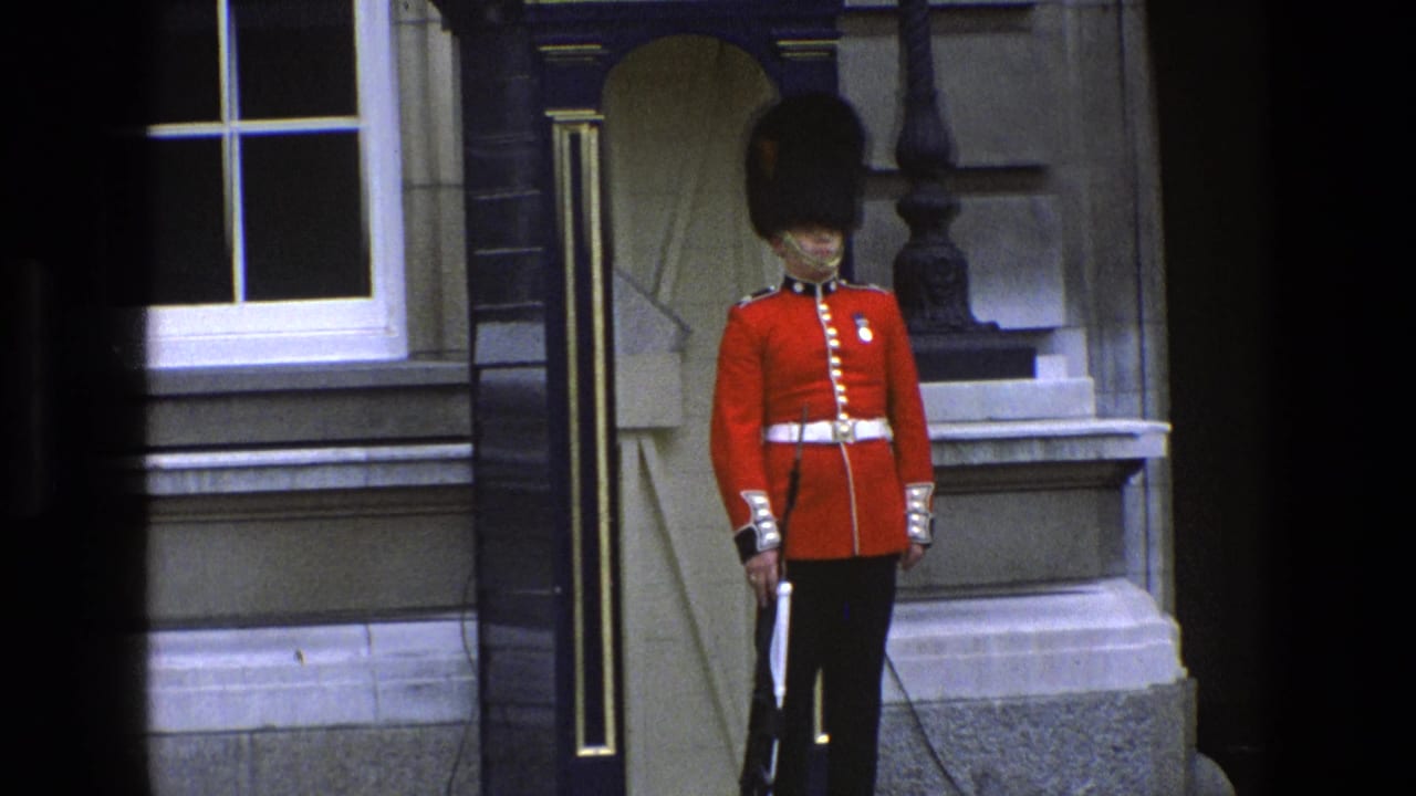 Royal guard in red tunic stands outside a stone building entrance.