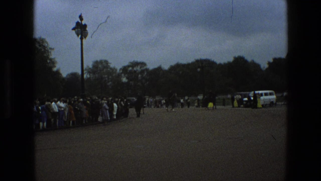 Crowd lines a paved park road as mounted police and vehicles appear in the distance.