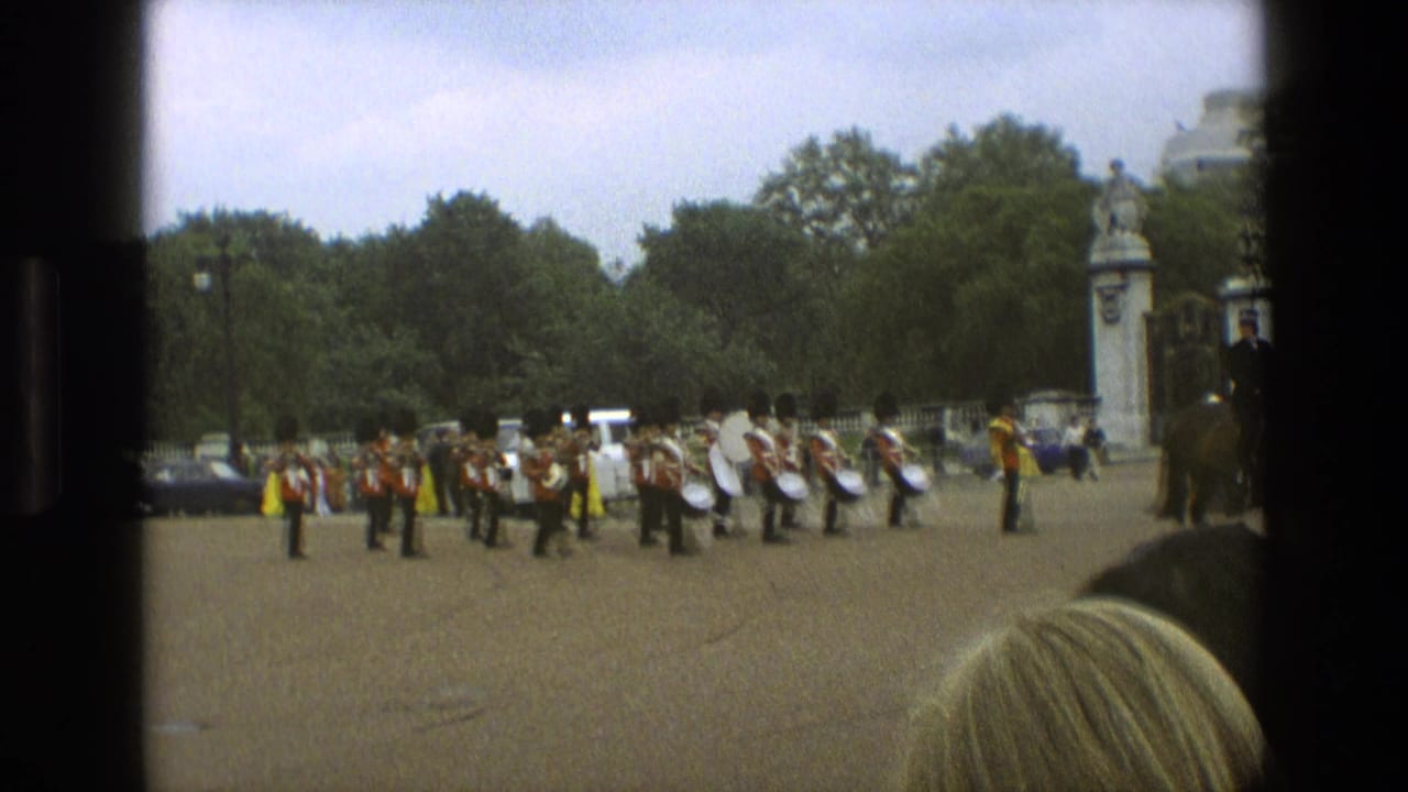 Guards in red tunics march across a paved square with drums and spectators nearby.