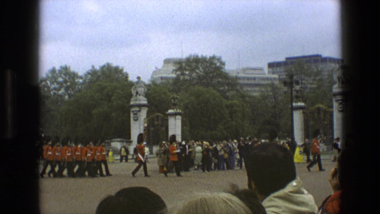 Guards in red uniforms march past spectators near ornate gates.
