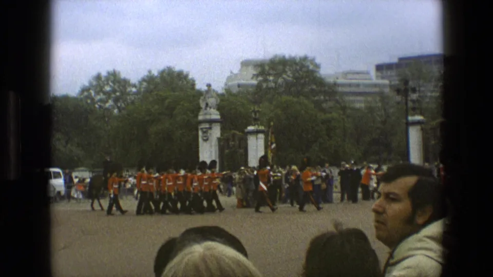1969 England frame with a formation of guards in red uniforms and bearskin hats moving across a public ceremonial space.