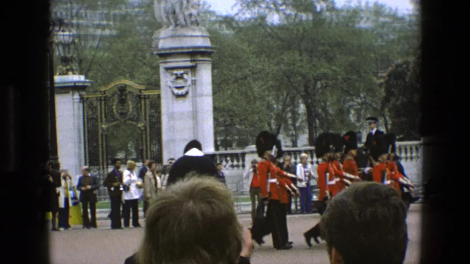 Mounted police on dark horses and guards in red tunics pass a royal-looking gate in this 1969 England home-movie frame.