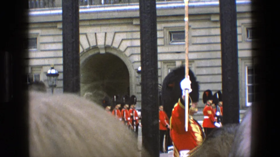 1969 England frame showing a ceremonial guard scene with spectators and an arched palace entrance visible through gate bars.