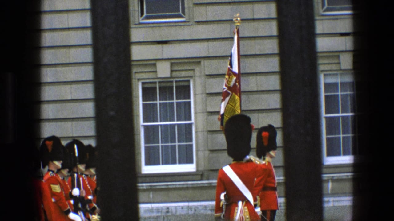 A red-coated guard stands near a royal flag while other guards gather by stone windows.