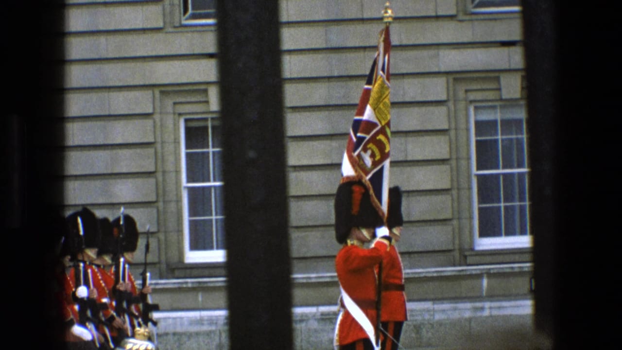 1969 England footage shows Grenadier Guards in ceremonial red tunics and bearskin hats near Buckingham Palace, partly obscured by dark bars.