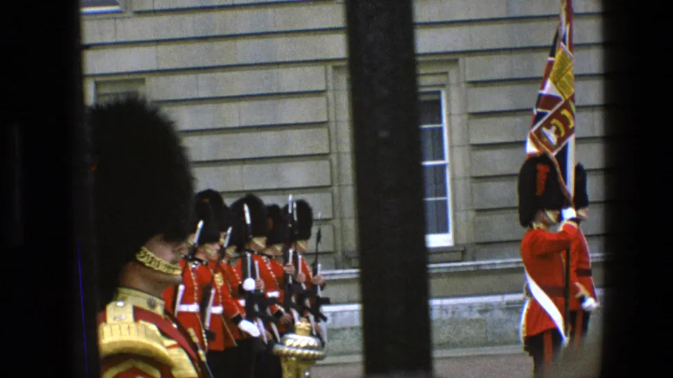 The final frame shows Buckingham Palace guards in red tunics and bearskin hats, with a foreground figure and dark bars cutting across the visitor view.