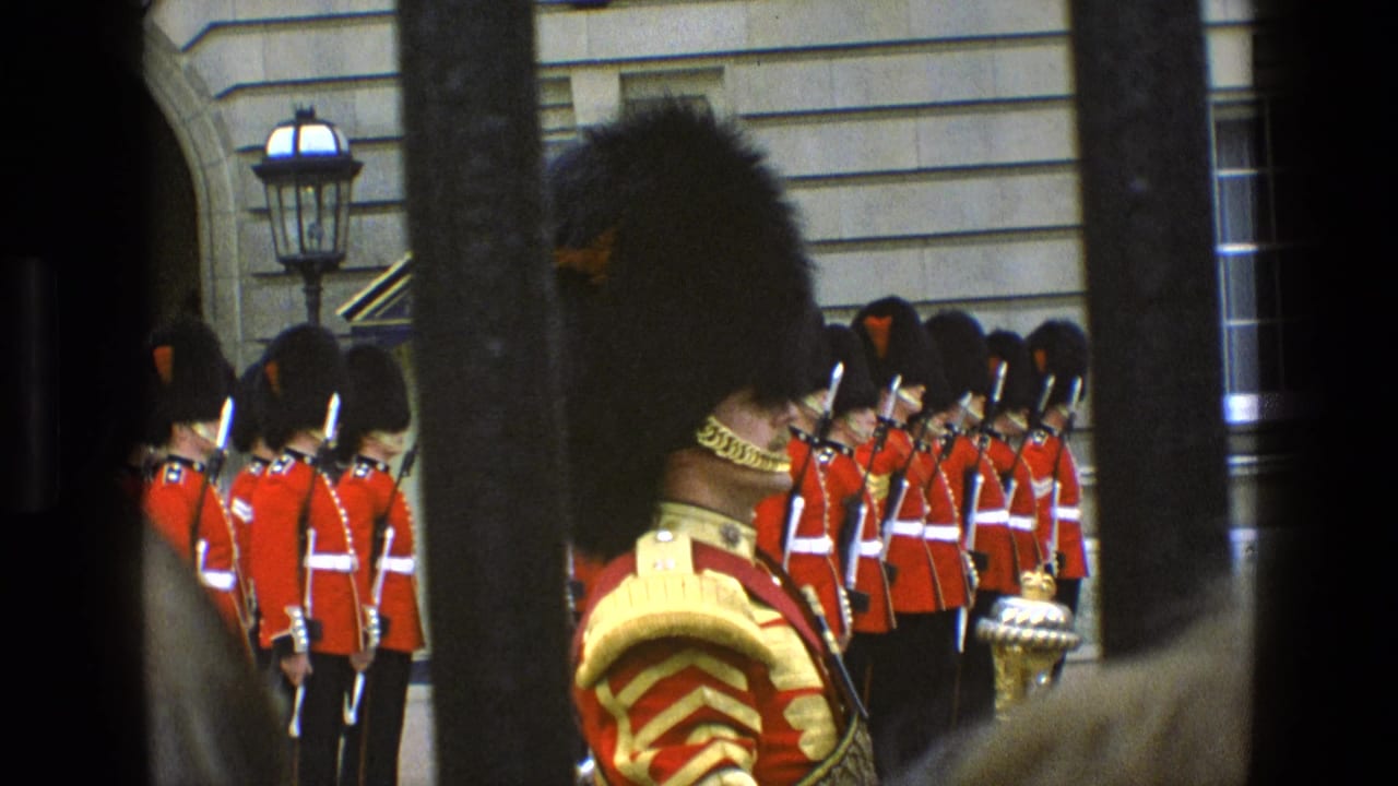 British guards in red tunics stand in formation behind dark vertical bars.